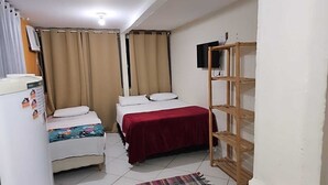 Ein kleines, kompaktes Zimmer mit zwei Betten, einer Holzregaleinheit, einem Kühlschrank und einem an der Wand befestigten Fernseher.