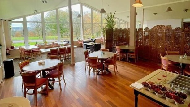 A spacious indoor area with multiple tables and chairs, large windows offering a view of the outdoors, and a variety of seating arrangements. - Fernhill Lodge Carrigaline (Carrigaline)