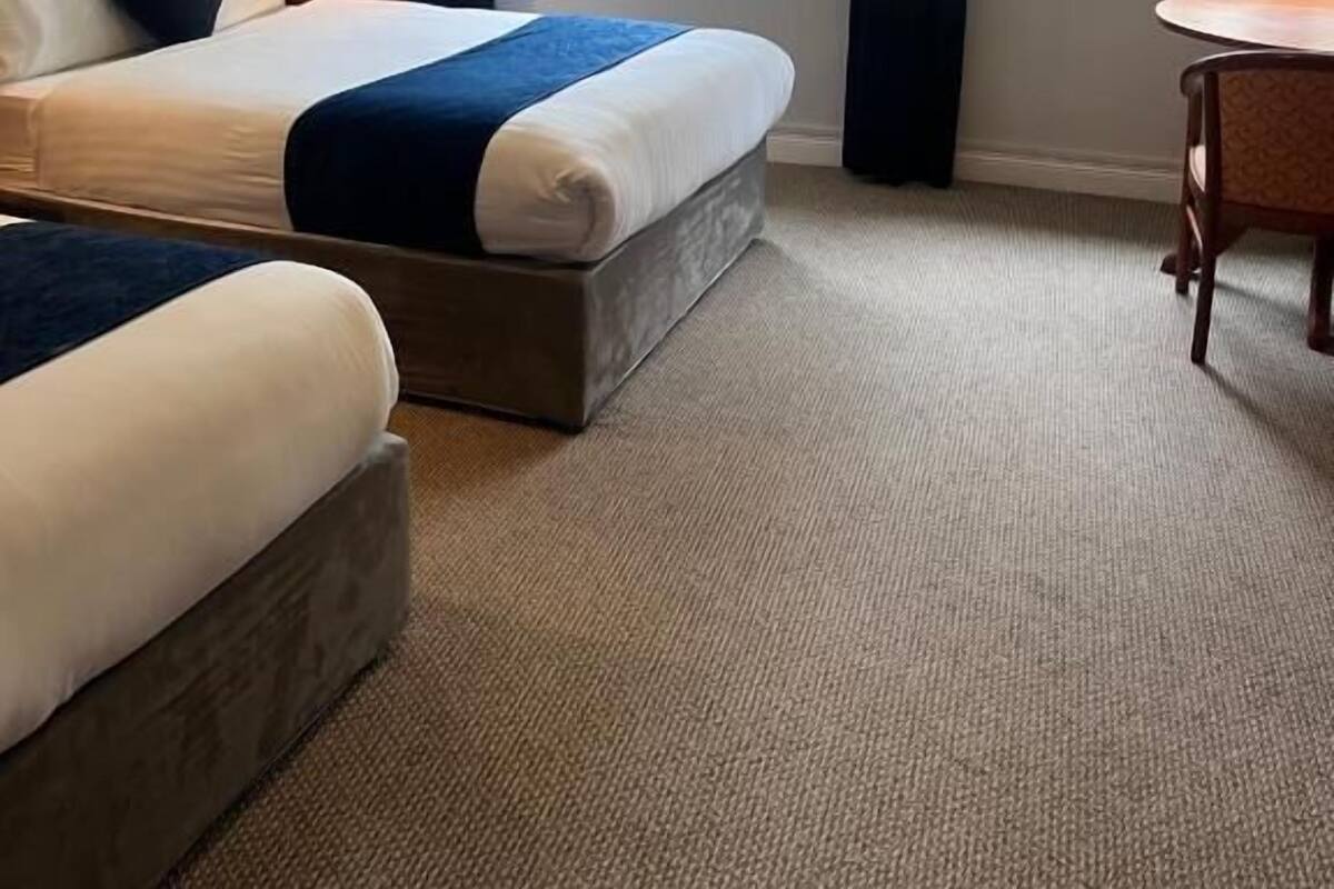 A hotel room with two beds, a small table, and a window with a view of trees.