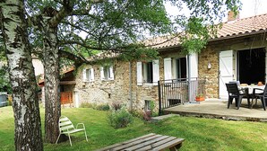 Una casa in pietra con un patio in legno, un tavolo da picnic e una sedia bianca nel giardino.