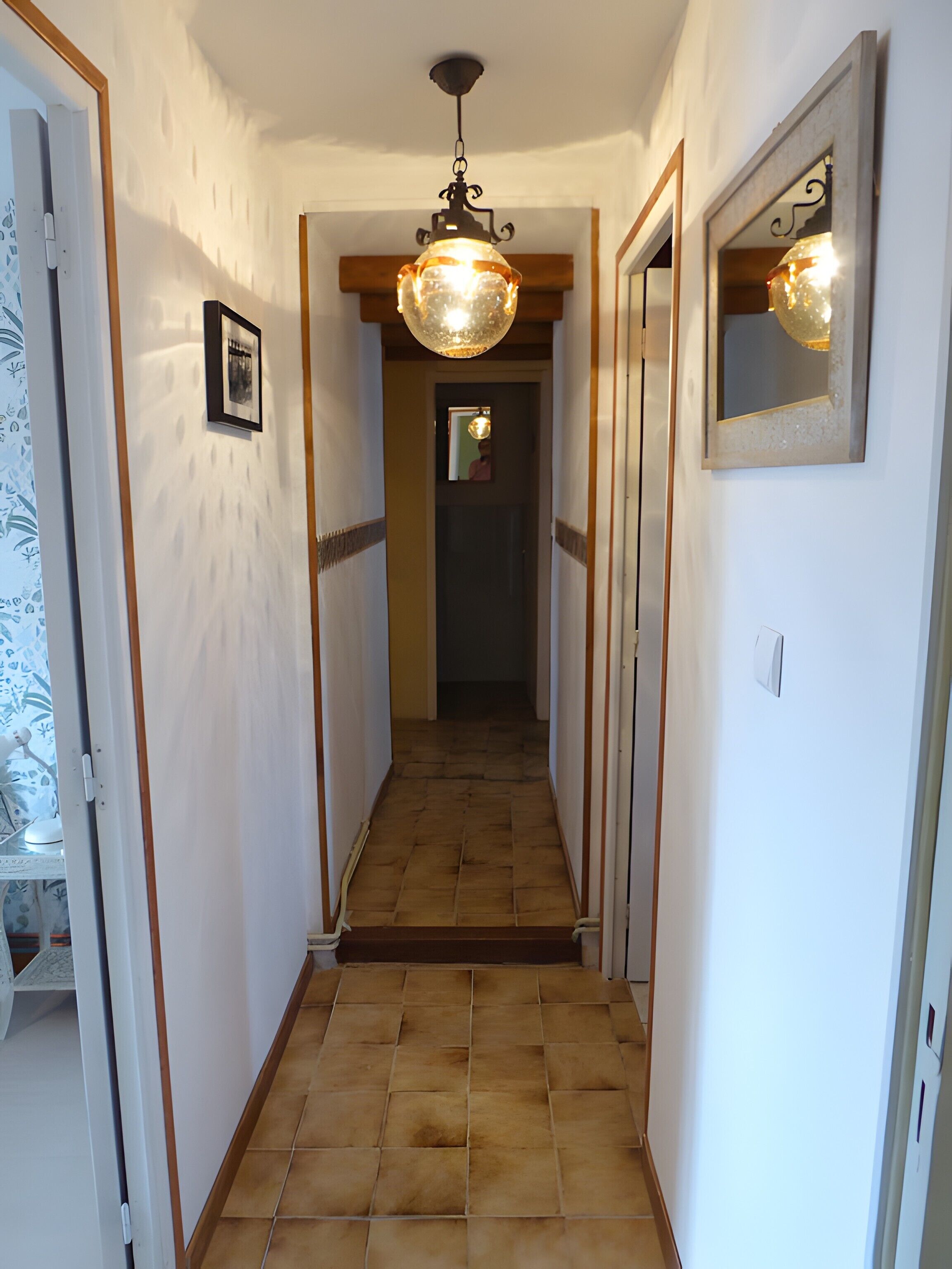 A hallway with a tiled floor, a hanging light fixture, and a framed picture on the wall.