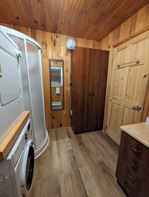 Ein gemütlicher Raum mit Holzbalkendecke, einer Tür mit Fenster, einer Waschmaschine und einem kleinen Schrank.