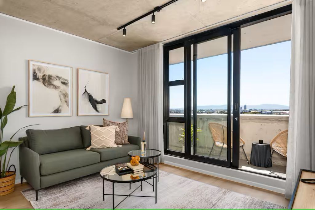 A modern living room with a sofa, a coffee table, and a large window with a view of the city.