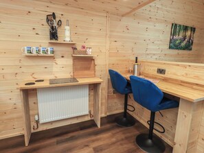 A wooden interior with a kitchen counter, two blue bar stools, a radiator, and a painting on the wall. - Bluebelle - Crossgate Luxury Glamping (Penrith)