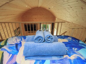 Ein gemütliches Schlafzimmer in einer Holzhütte mit Bett, zusammengerollten Handtüchern und einem Fenster.