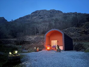 A rustic, arched building with a gravel driveway leading to a wooden door, surrounded by a mountainous landscape. - Bluebelle - Crossgate Luxury Glamping (Penrith)