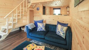 Ein Holzblockbau-Innenraum mit Treppe, einem blauen Sofa und einem Schlafzimmer auf dem Dachboden.