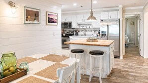 A modern kitchen with white cabinetry, a wooden island, bar stools, and a dining table with placemats. - Beachfront Escape | Walk to Trading Post | 4BR (Port St. Joe)