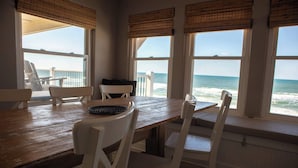 A dining area with a wooden table and white chairs, overlooking the ocean. - Rehab- Beach front, Sleeps 9 (Port St. Joe)