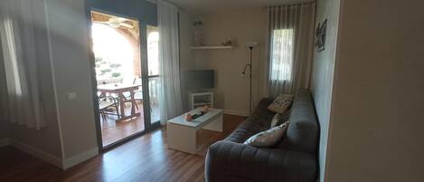 A living room with a sofa, a coffee table, a TV, and a dining area with chairs and a table.