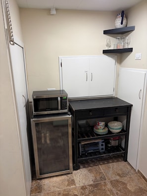 A compact kitchen with a refrigerator, microwave, oven, and a small shelf with dishes.