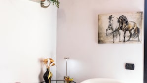 A living room with a glass coffee table, a vase with dried flowers, a painting of horses, and a modern floor lamp.