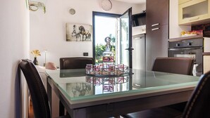 A modern kitchen with a glass dining table, dark cabinetry, and a view through an open door.