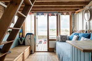 Een houten interieur met een bed, een tafel en uitzicht op het strand.