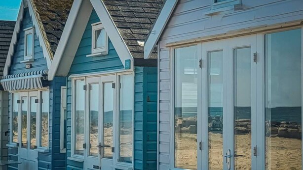 Una serie di casette sul mare con finestre a cornice bianca e tetto in legno.