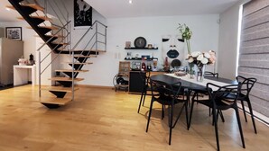 A modern interior with a spiral staircase, a dining area with black chairs, and a kitchen in the background.