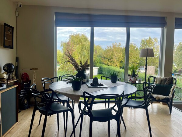 A dining area with a round table, chairs, potted plants, and a view of a garden through large windows.