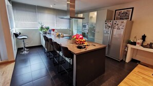 A modern kitchen with a central island, bar stools, a refrigerator, and a dining area.