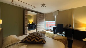 A hotel room with a bed, a desk, a chair, a mirror, and a view of the outside.