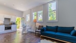 En rummelig opholdsstue med sofa, spisebord med stole og et køkken i baggrunden.