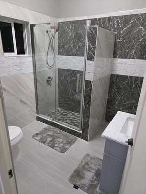 Ein modernes Badezimmer mit einer Duschkabine, einem weißen Waschbecken und einer Toilette.