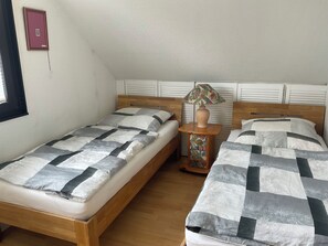 Un dormitorio con dos camas, una mesita de noche con lámpara y una ventana.