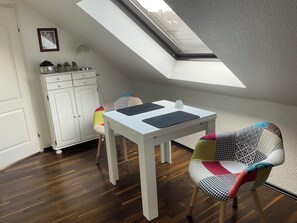 Una habitación con tragaluz, una mesa blanca con manteles individuales negros, una silla estampada y un armario blanco.