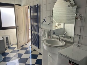 Un baño con piso a cuadros, un lavamanos, un espejo, un perchero y una ventana con cortinas.