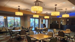 Un restaurante con varias mesas y sillas, iluminación colgante y vistas amplias a través de grandes ventanales.