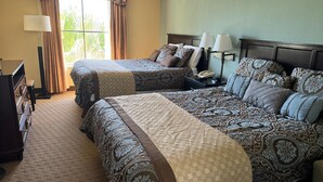 Una habitación de hotel con dos camas, un aparador, una mesita de noche y un ventanal con cortinas.