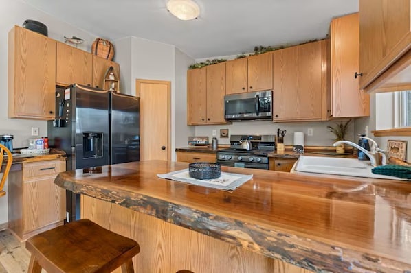 A kitchen with wooden cabinets, a stainless steel refrigerator, a microwave, and a wooden countertop.