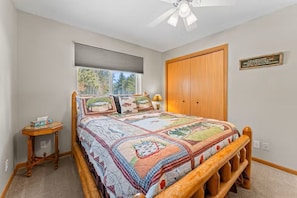 A bedroom with a wooden bed, a window with blinds, a ceiling fan, and a wooden wardrobe.