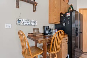A kitchen with wooden cabinets, a black refrigerator, a coffee maker, and a sign on the wall.