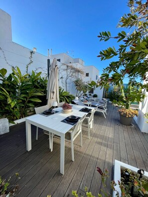 Eine Dachterrasse mit weißem Esstisch, umgeben von Topfpflanzen und blauem Himmel.