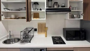 A modern kitchen with a stainless steel sink, a black stove, a microwave, and open cabinets with kitchenware. - Cosy & Chic Apartment with Secure Parking in the Heart of Casablanca (Dar-el-Beida)