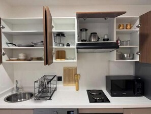 A modern kitchen with a stainless steel sink, a black stove, a microwave, and open cabinets with kitchenware. - Cosy & Chic Apartment with Secure Parking in the Heart of Casablanca (Dar-el-Beida)