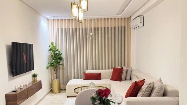 A modern living room with a sofa, a dining table set for four, and a TV mounted on the wall. - Cosy & Chic Apartment with Secure Parking in the Heart of Casablanca (Dar-el-Beida)