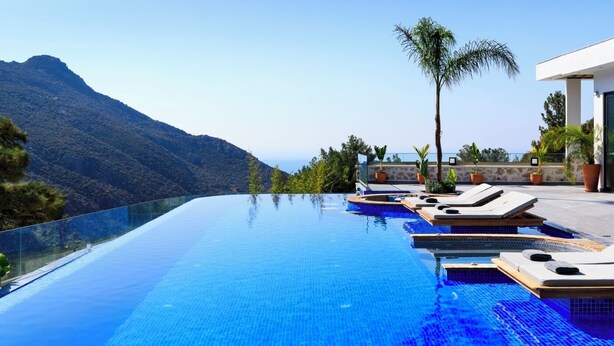 A infinity pool with a mountain view, lounge chairs, and potted plants. - Villa Sade: A Modern Luxury Retreat with Infinity Pool and Sweeping Views (Kaş/Antalya)