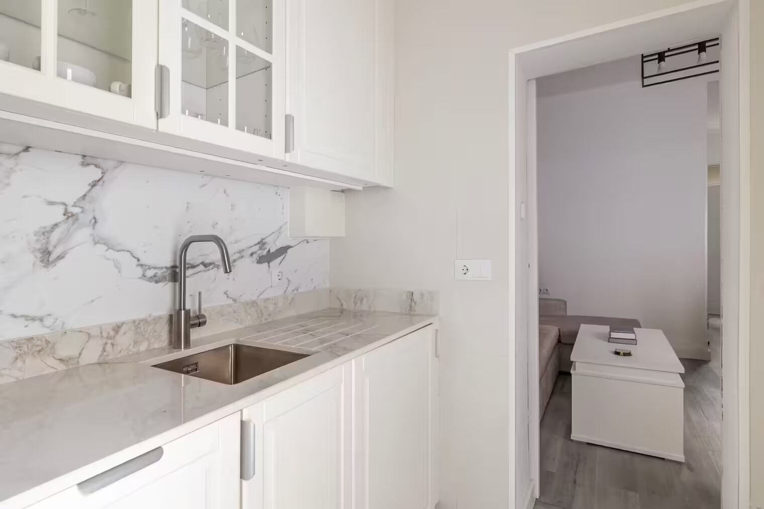 A modern kitchen with white cabinetry, a marble backsplash, and a sink.