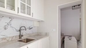 Una cocina moderna con armarios blancos, salpicadero de mármol y un lavamanos.