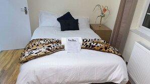 A neatly made bed with a leopard print bedspread, a white pillow, and a 'hello.' sign on the bed. - Central 1 Bed Apartment - Sleeps 2 With Wifi (Wellingborough)