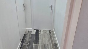 A narrow hallway with a white door at the end, a tiled floor, and a white wall. - Central 1 Bed Apartment - Sleeps 2 With Wifi (Wellingborough)