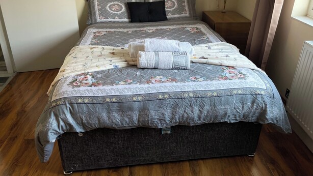 A bed with a floral-patterned duvet, a black pillow, and neatly folded towels. - Central 1 Bed Apartment - Sleeps 2 With Wifi (Wellingborough)