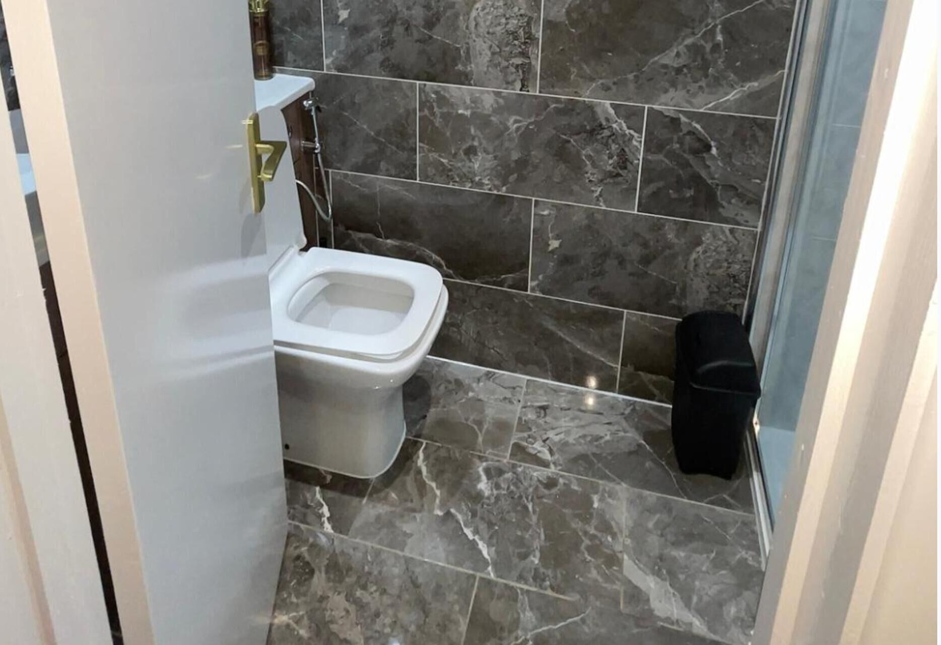 A bathroom with a toilet, marble tiles, and a trash bin