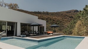 A modern outdoor pool area with lounge chairs and umbrellas, surrounded by a hillside. - Quinta Real San Carlos (Santiago)