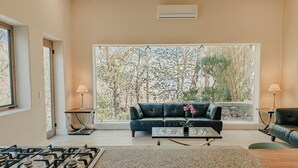 A living room with a sofa, a coffee table, a gas stove, and a large window with a view of trees. - Quinta Real San Carlos (Santiago)
