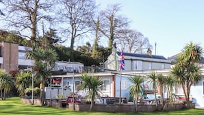 A building with a flag, surrounded by palm trees and a grassy area. - Sea Glimpse (Dawlish)