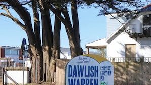A sign for Dawlish Warren with a bicycle symbol, a bus symbol, and a car symbol, indicating public transport options. - Sea Glimpse (Dawlish)