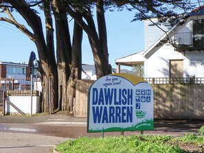 A sign for Dawlish Warren with a bicycle symbol, a bus symbol, and a car symbol, indicating public transport options. - Sea Glimpse (Dawlish)