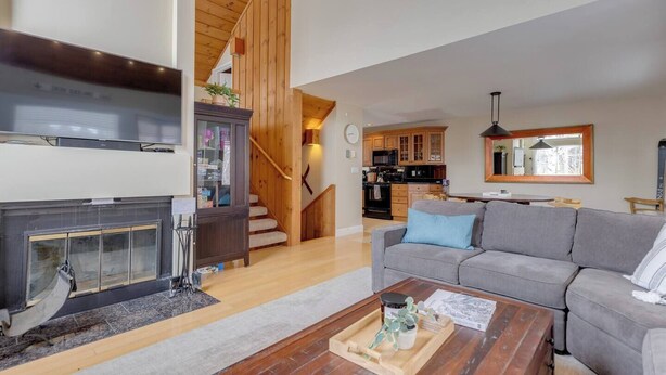 A living room with a fireplace, a sofa, a coffee table, and a kitchen in the background. - Modern Mountain Getaway at Loon (Lincoln)